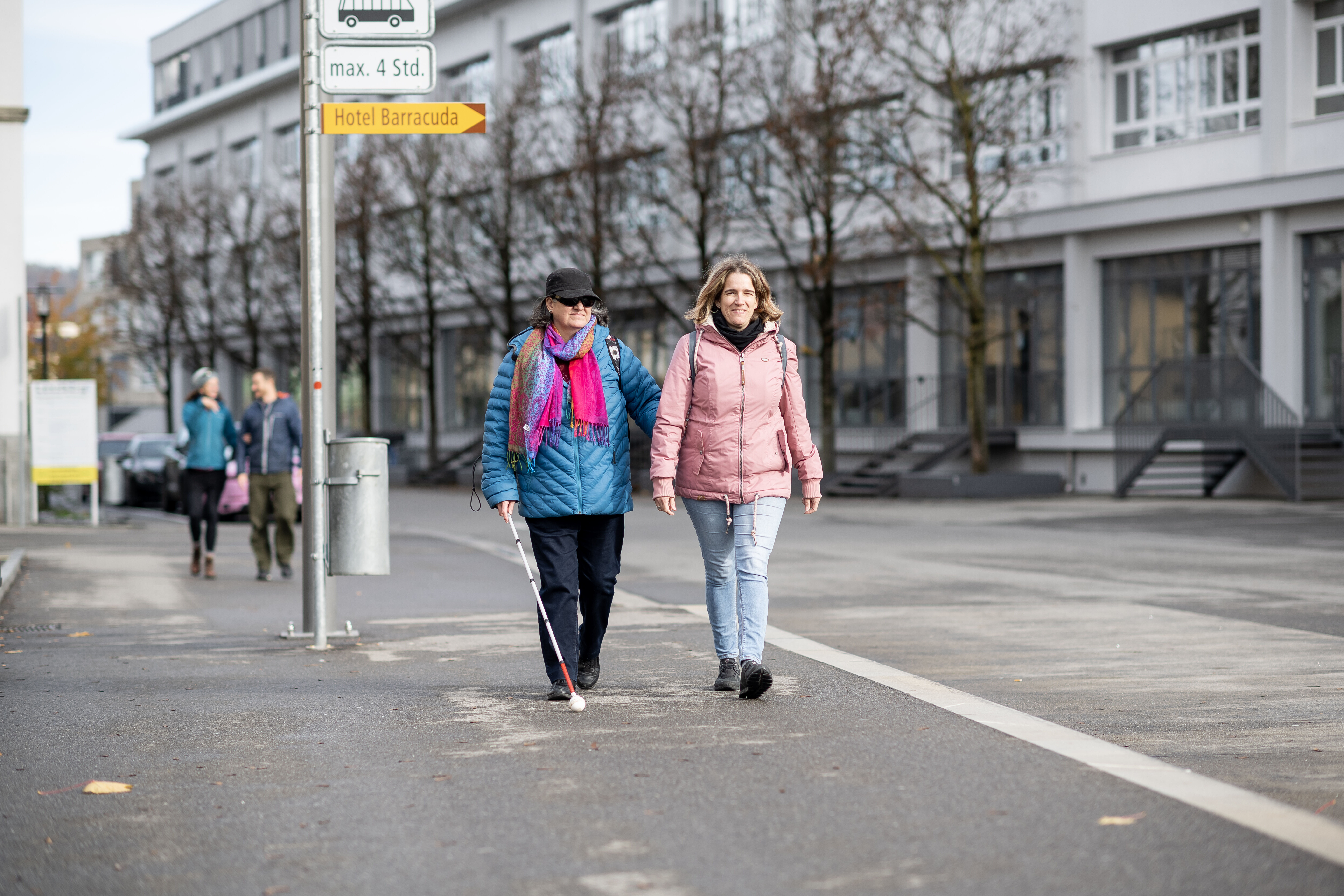 Deux femmes marchent sur un chemin. Une femme utilise une canne blanche.